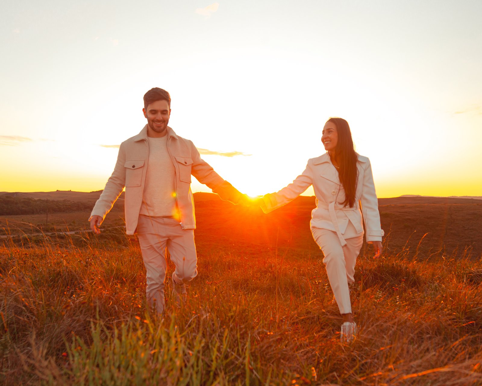 Casal caminhando de mãos dadas em campo ao entardecer